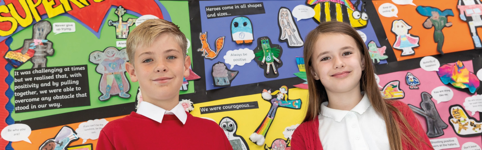 Two Miers Court pupils smile at the camera in front of a display reading "Positivity is our Superpower"